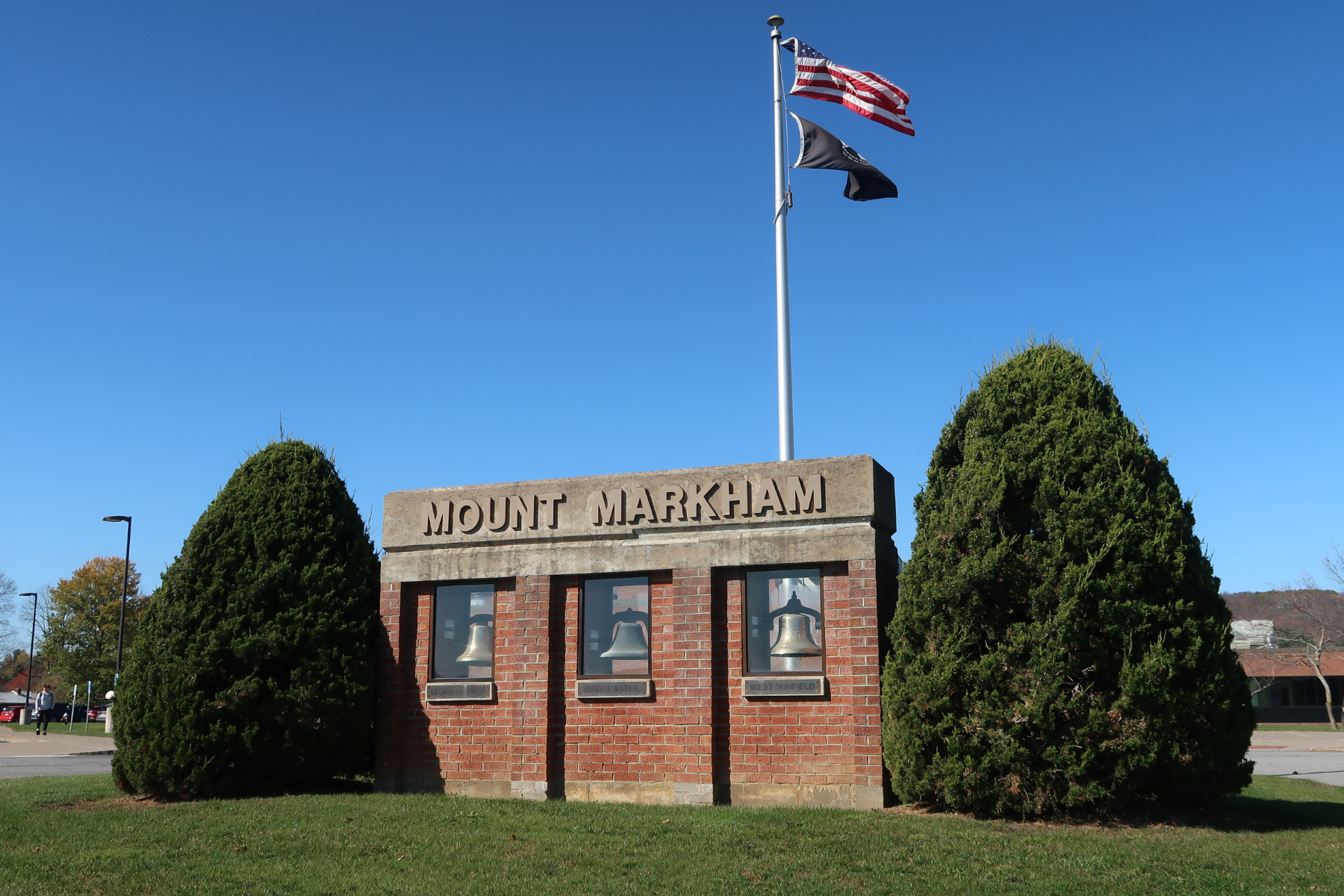 A brick structure with school bells and Mount Markham engraved on top under a blue sky.